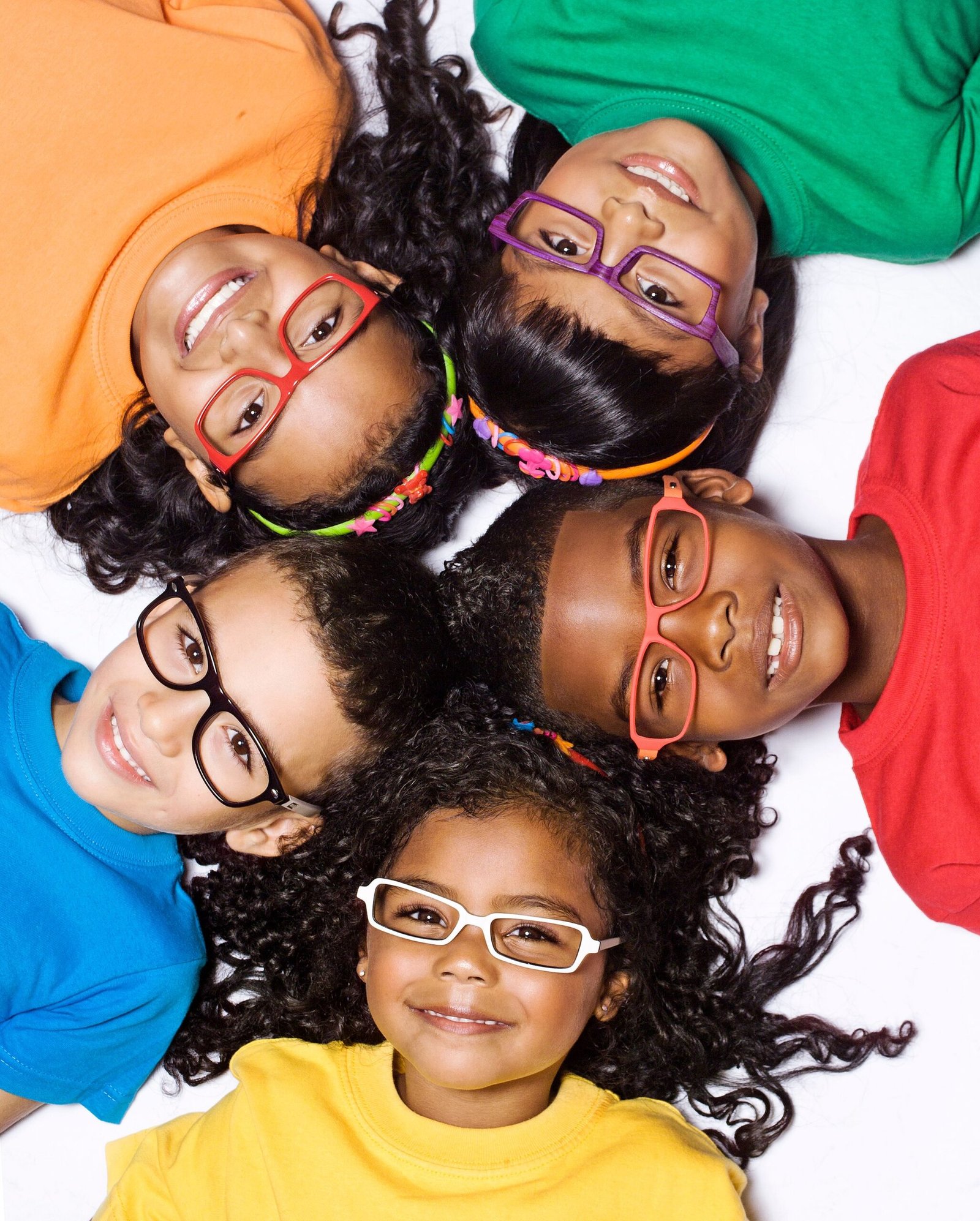 Five smiling children lying in colorful shirts and glasses, showcasing diversity and joy.